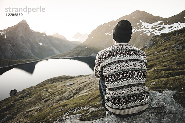 Kaukasischer Mann sitzt auf einem Felsen und bewundert die malerische Aussicht auf einen Bergsee