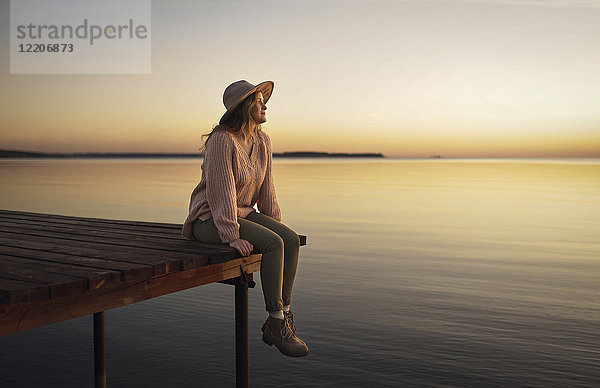 Caucasian woman sitting on dock of lake admiring sunset