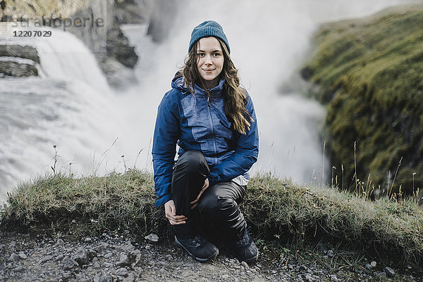 Porträt einer lächelnden kaukasischen Frau  die in der Nähe eines Wasserfalls sitzt