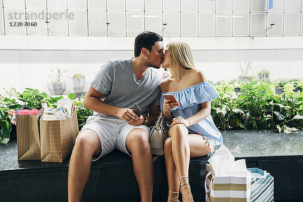 Caucasian couple with shopping bags and cell phones kissing