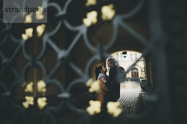 Caucasian couple embracing in street behind gate