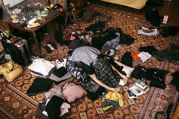 Caucasian man sitting on messy floor with shirt covering head