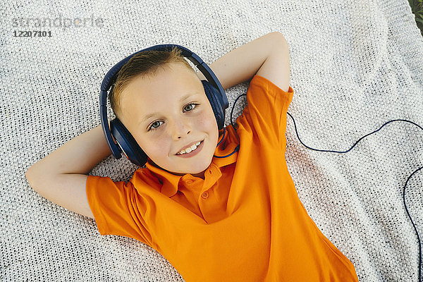 Smiling Caucasian boy laying on blanket in park listening to headphones