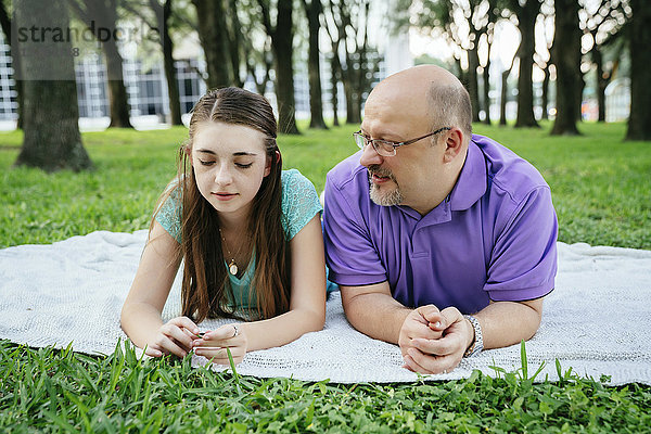 Serious Caucasian father and daughter talking on blanket in park