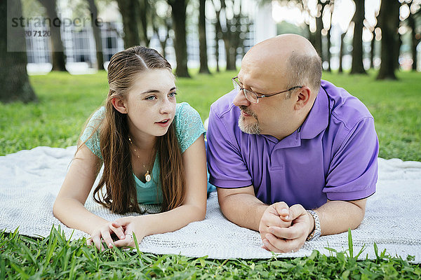 Serious Caucasian father and daughter talking on blanket in park
