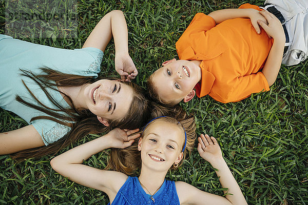 Close up portrait of smiling Caucasian brother and sisters laying on grass