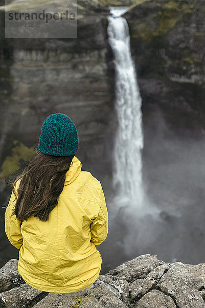 Kaukasische Frau sitzt auf einer Klippe und bewundert einen Wasserfall