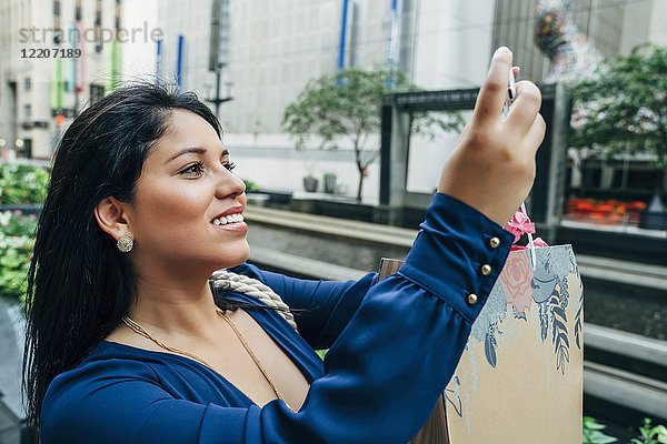 Hispanic woman with shopping bag posing for cell phone selfie