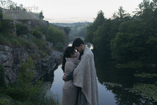 Caucasian couple wrapped in blanket hugging near river