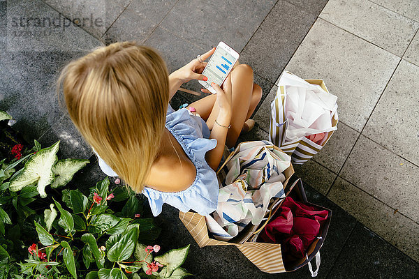 High angle view of Caucasian woman with shopping bags texting on cell phone