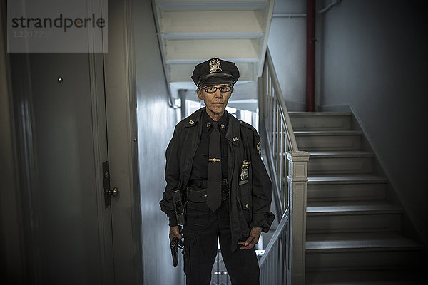 Portrait of older Caucasian policewoman holding gun in apartment staircase