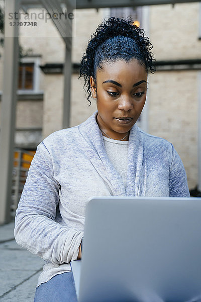 Serious Black woman using laptop outdoors