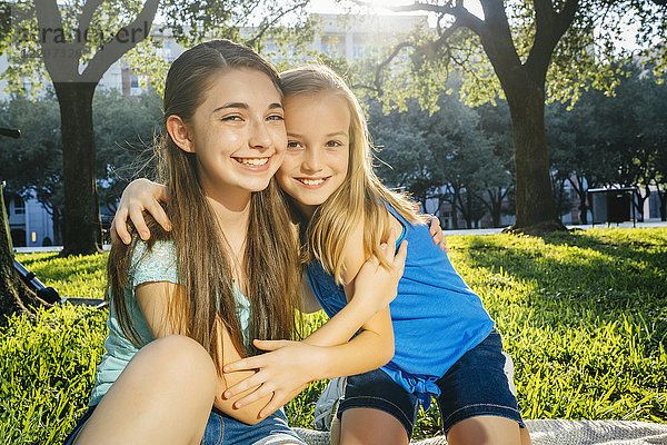 Portrait of smiling Caucasian sisters hugging in park
