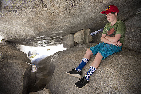 Pensive Caucasian boy sitting on rocks