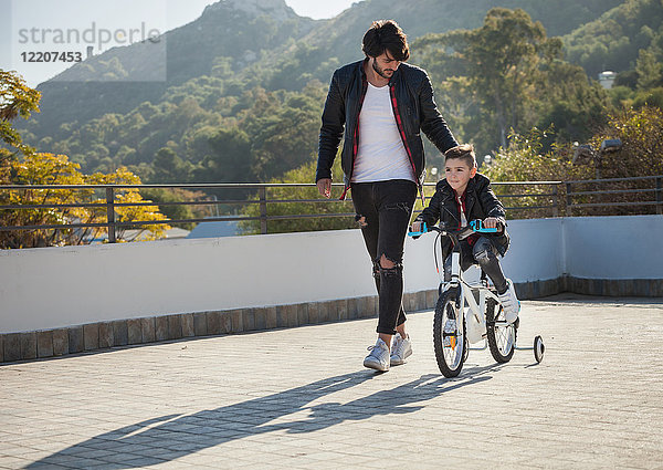 Junge Junge fährt Fahrrad mit Stabilisatoren  Vater geht neben ihm