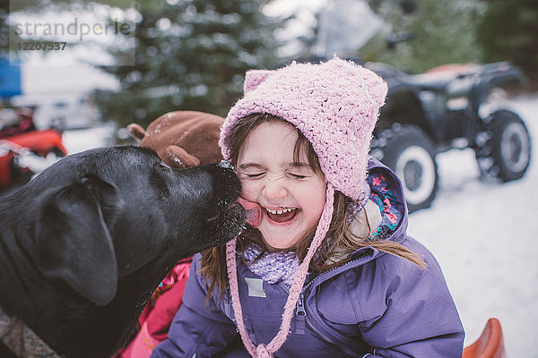 Junges Mädchen mit Hund in verschneiter Landschaft  Hund leckt Mädchen das Gesicht