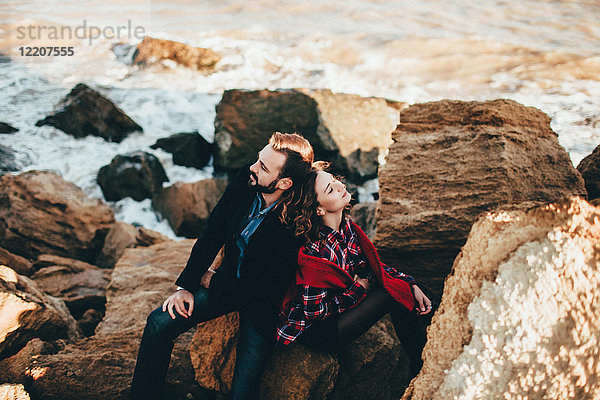 Romantisches Paar mittlerer Erwachsener  die Rücken an Rücken auf einem Strandfelsen sitzen  Oblast Odessa  Ukraine