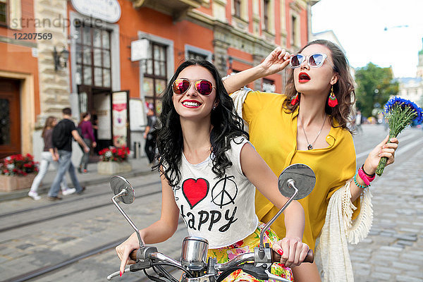 Porträt von zwei glücklichen Freundinnen mit Sonnenbrille auf dem Roller auf einer gepflasterten Straße  Odessa  Ukraine
