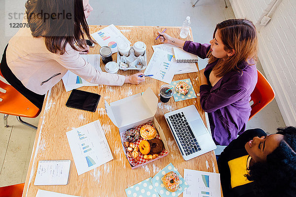 Kollegen arbeiten am Schreibtisch zusammen und teilen sich Doughnuts