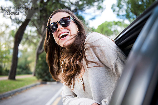 Glückliche junge Frau auf Autoreise lehnt sich aus dem Autofenster