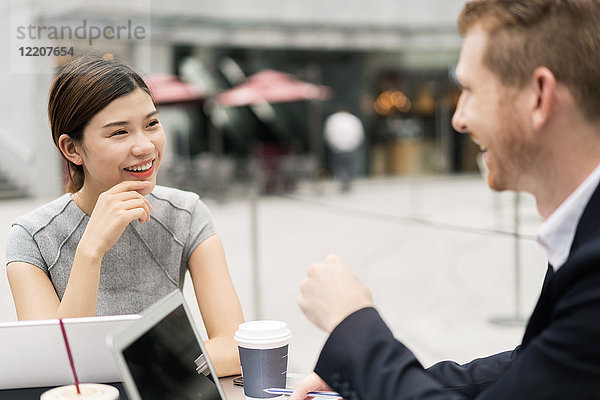 Junge Geschäftsfrau und Mann diskutieren im Straßencafé