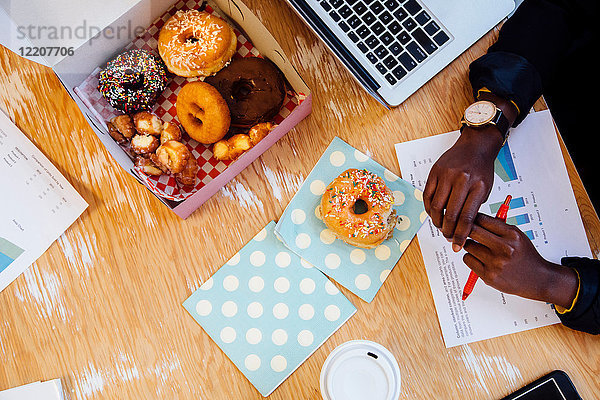 Geschnittene Draufsicht einer Kuchenschachtel mit Donuts auf dem Schreibtisch der Frau