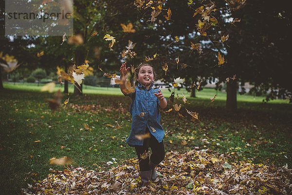 Mädchen im Park wirft Herbstblätter