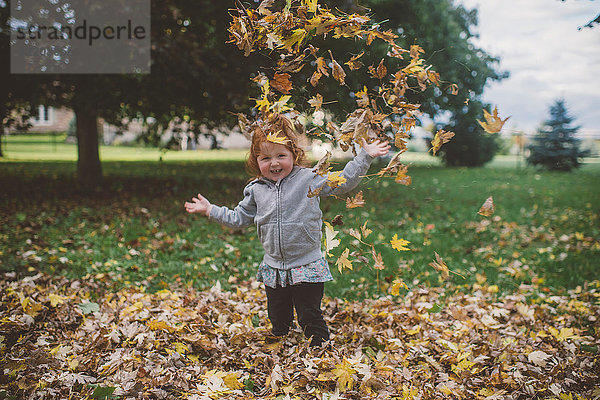 Porträt eines rothaarigen weiblichen Kleinkindes im Park  das Herbstblätter wirft