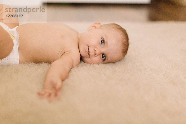 Porträt eines süßen Mädchens in Windel auf beigem Teppich liegend