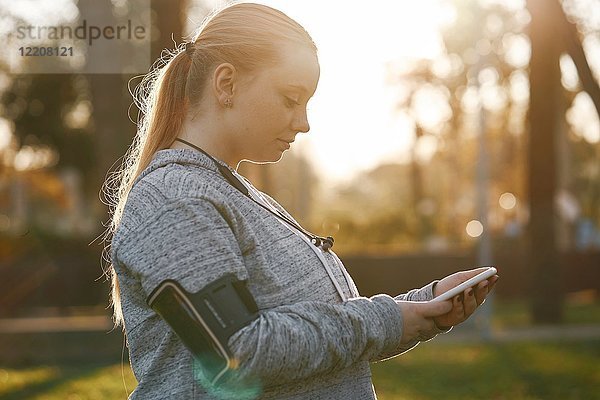 Kurvenreiche junge Frau trainiert im Park und sieht sich ein Smartphone an