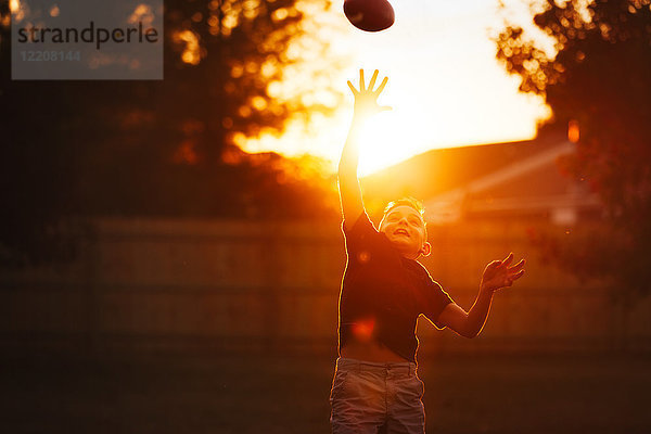 Junge übt American Football im Garten und fängt den Ball bei Sonnenuntergang mitten in der Luft