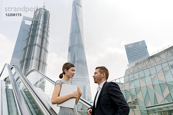 Junger Geschäftsmann und junge Geschäftsfrau bewegen sich auf der Rolltreppe im Finanzzentrum Shanghai  Shanghai  China