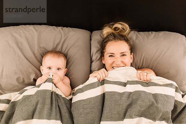 Porträt einer im Bett unter der Bettdecke liegenden Frau mit Baby-Tochter  Draufsicht