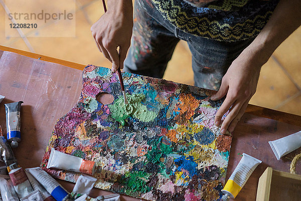 Männlicher Künstler beim Mischen von Ölfarbe auf der Palette im Künstleratelier  mittlerer Abschnitt