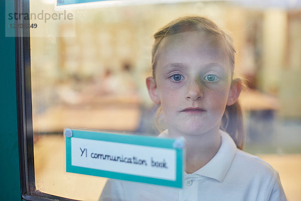 Porträt einer Schülerin  die in der Grundschule durch ein Klassenzimmerfenster schaut