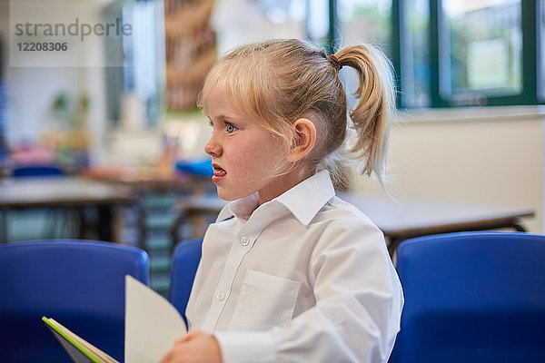 Schulmädchen zieht in der Grundschule in der Klasse ein Gesicht