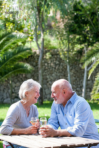 Älteres Ehepaar sitzt im Garten und genießt ein Glas Wein