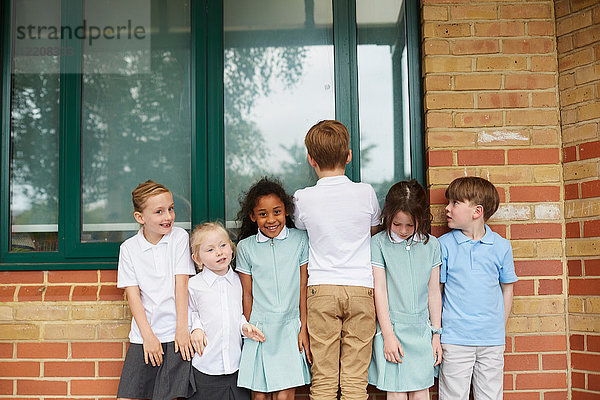 Schulmädchen und Jungen stehen in einer Reihe vor dem Grundschulgebäude  Porträt