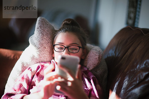 Mädchen entspannt sich auf dem Sofa und schaut auf ein Smartphone