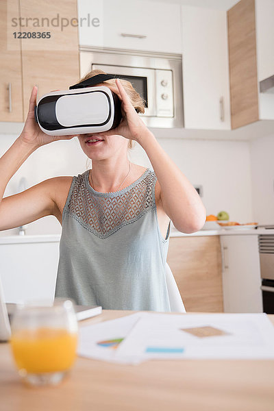 Junge Frau schaut durch ein Virtual-Reality-Headset am Küchentisch