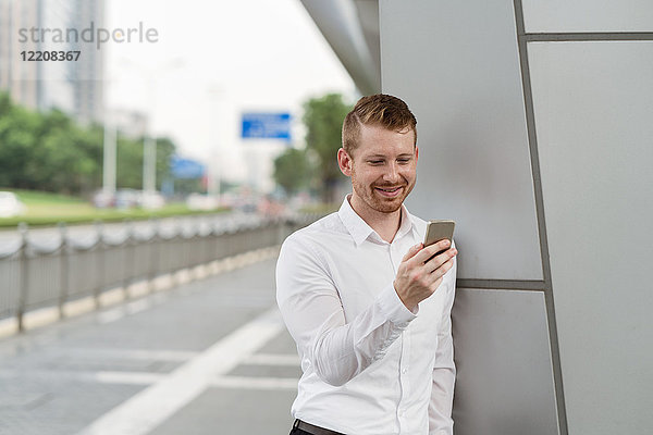 Junger Geschäftsmann betrachtet den Touchscreen eines Smartphones in einer Stadt  Shanghai  China