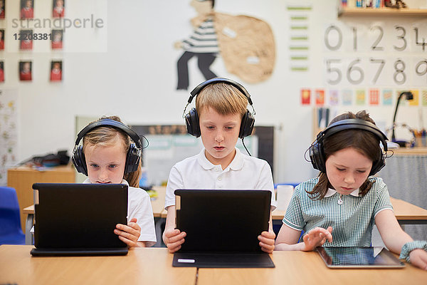 Schüler und Mädchen hören in der Grundschule Kopfhörer im Unterricht