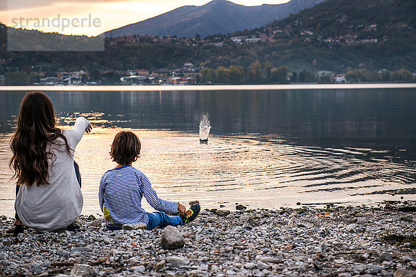 Rückansicht eines Jungen und einer jungen Frau  die in der Abenddämmerung Kieselsteine in den Fluss werfen  Vercurago  Lombardei  Italien
