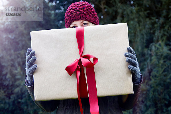 Frau hält Weihnachtsgeschenk mit roter Schleife hoch