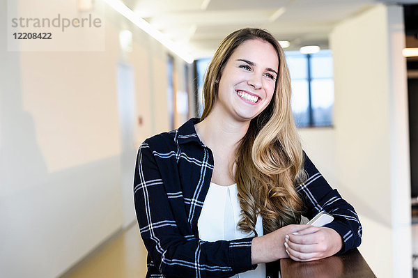 Porträt einer glücklichen jungen Geschäftsfrau mit einem Smartphone im Büro-Atrium