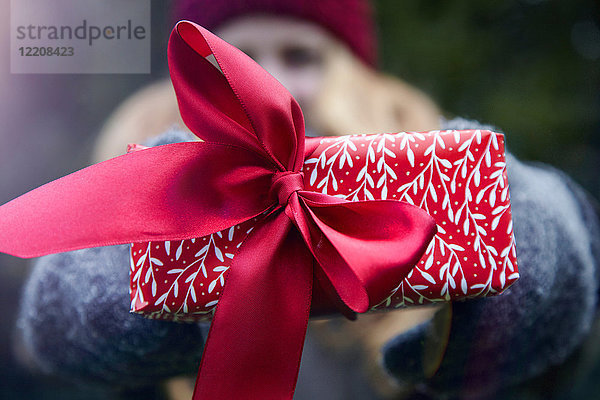 Frau hält Weihnachtsgeschenk mit roter Schleife hoch