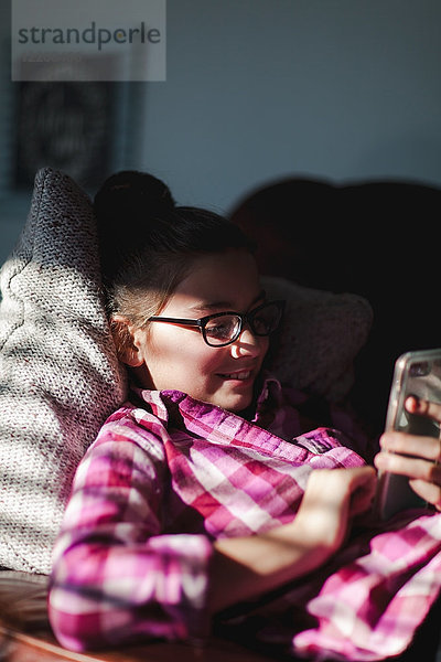 Mädchen entspannt sich auf dem Sofa und schaut auf ein Smartphone