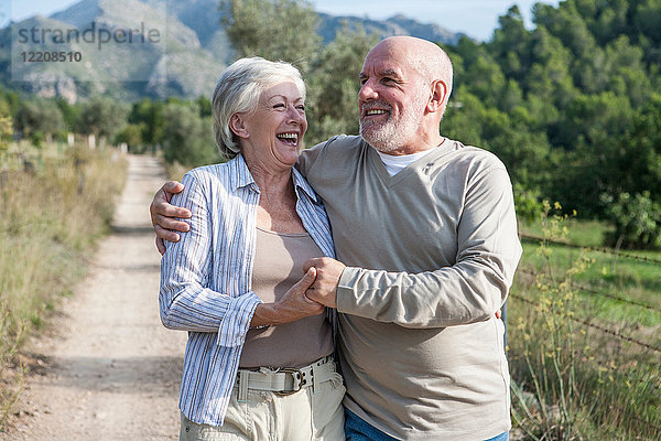Älteres Ehepaar beim gemeinsamen Spaziergang in ländlicher Umgebung  Händchen haltend  lächelnd