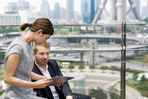 Junge Geschäftsfrau und Mann betrachten digitales Tablet im Bürgersteig-Café im Finanzzentrum von Shanghai  Shanghai  China