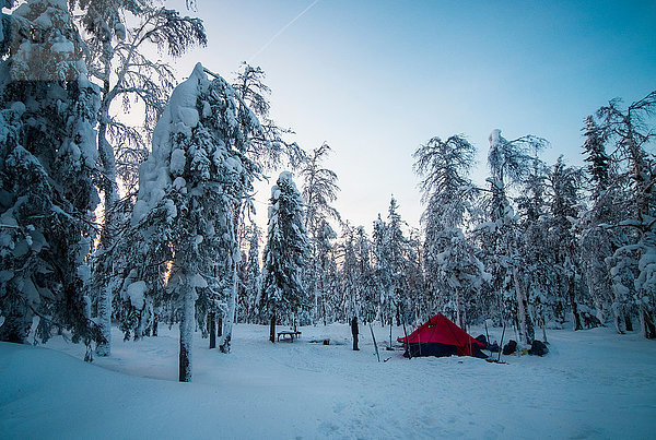 Mann steht neben Zelt im verschneiten Wald  Russland